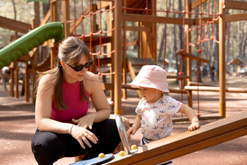 Obraz premium happy mother plays and pushes her child on a swing in the park on a hot spring day