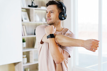 A man takes a break to stretch his arm, using the support of headphones to enhance his workout in a...