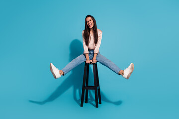 Full length photo of good mood carefree woman wear silky blouse riding stool having fun isolated blue color background - obrazy, fototapety, plakaty