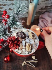 Cup of christmas hot cocoa with marshmallows and cinnamon on a table with christmas tree pine candles