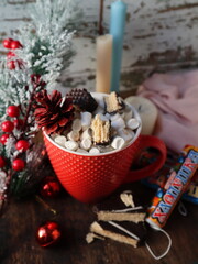 Cup of christmas hot cocoa with marshmallows and cinnamon on a table with christmas tree pine candles