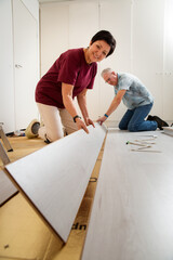 Senior couple installing laminate flooring in their new home together. DIY concept. Mature woman and man are doing renovation.