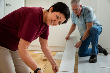 Senior couple installing laminate flooring in their new home together. DIY concept. Mature woman and man are doing renovation.