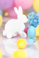 A figurine of a white Easter bunny against a background of Easter eggs, multi-colored pastel balls and blue hydrangeas