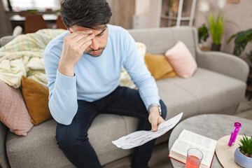 worried man sitting on couch looking at bills