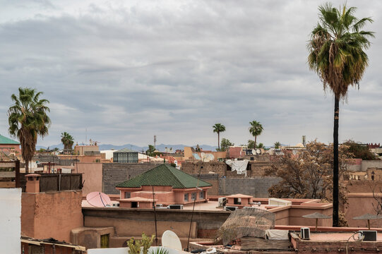 View of the roofs of the Medina in Marrakech, Morocco. Lots of satellite dishes and palm trees can be seen, with the Atlas mountains in the distance.