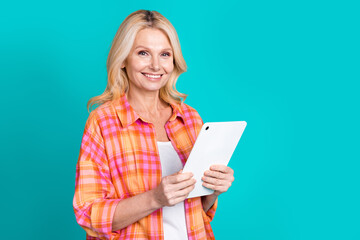 Portrait of good mood smart woman with straight hair dressed plaid shirt holding tablet in arms isolated on turquoise color background