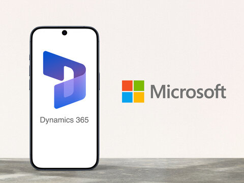 Dynamics 365 Logo is displayed on a modern smartphone standing on a desk, Microsoft logo next to it, enterprise resource planning (ERP) and customer relations management