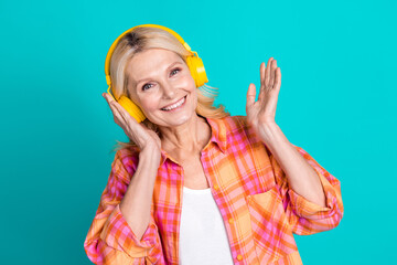 Portrait of satisfied woman straight hair dressed plaid shirt touch headphones raising palm up isolated on turquoise color background