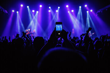 Holding a phone and taking photos of the concert. Concert background.