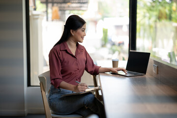 A diligent professional woman works on her laptop in a well-lit cafe, with a coffee cup and...