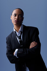 A young African American woman confidently poses in a suit and tie in a photography studio.