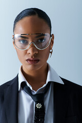 Young African American woman in 20s, confidently wearing suit, tie, glasses in studio.