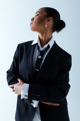 Confident young African American woman in her 20s, standing with arms crossed in a suit and tie.