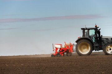 Farmer with tractor seeding crops at field - 777309461