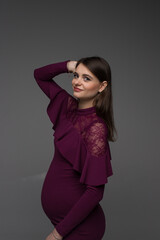 portrait of a pregnant woman in a purple dress on a grey background