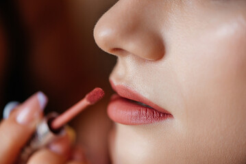 A close-up shot of a bride's lips being carefully painted with lipstick by a makeup artist