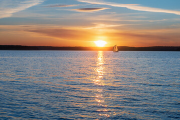 Fototapeta premium A sailing yacht against the background of the setting sun. Calming water evening landscape
