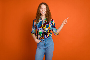 Photo of lovely cute girl wear trendy print clothes recommend empty space isolated on vivid orange color background