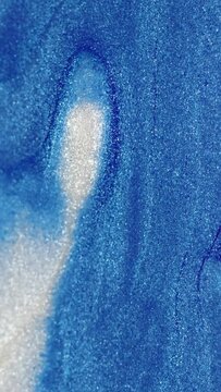 Vertical video. Wet glitter texture. Metallic ink flow. Blue white color shimmering paint fluid wave motion on blur art abstract background with free space.