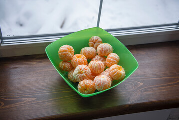 A bowl of peeled oranges sits on a wooden table. The peeled oranges are ripe and ready to eat. The scene is cozy and inviting, with the oranges adding a pop of color to the room
