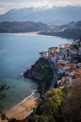 Scenic view captures Lastres coastal allure, with snowy peaks and azure sea.