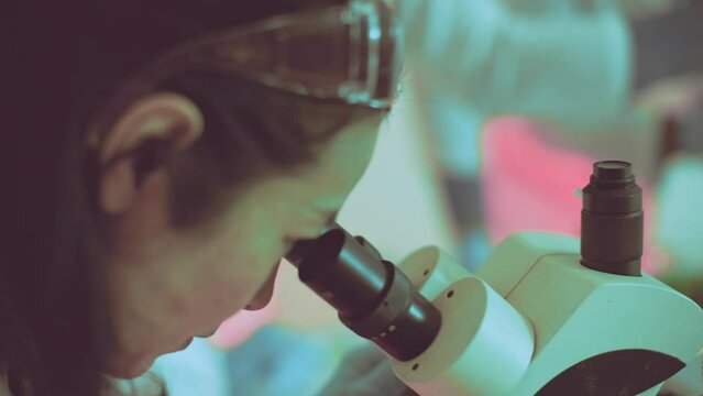 scientist intently studies a sample through a microscope in a lab setting - Focused researcher equipped with safety eyewear, representing precision in scientific investigation and education