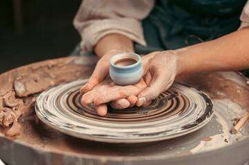 A person is holding a ceramic cup in their hands while working on a pottery wheel. Concept of...