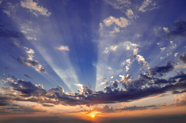 The sky is blue with a few clouds and the sun is setting. The sun is shining through the clouds,...