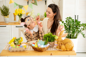 Easter family traditions. A young mother and daughter are playing with colorful eggs in the kitchen, enjoying the holiday, the family is preparing for a bright Easter by painting eggs