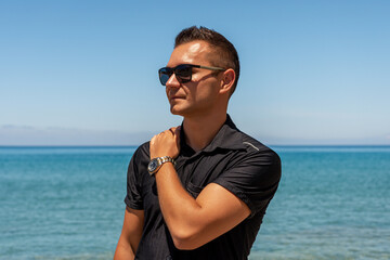 Attractive man in black shirt on sea background. Summer vacation. - Powered by Adobe