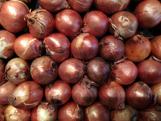 Obraz premium Fresh onions on the table in the store, close-up. Vitamin seasoning for a healthy diet. A spicy food ingredient. A slide, a bunch of onions. Market tent, retail and wholesale. Trading place, market. A