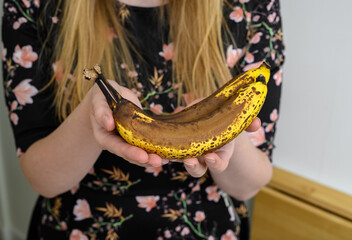 Dwa dojrzałe banany z ciemną skórką trzymane w rękach przez kobietę 