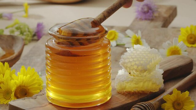 Drops of honey slowly flowing from a wooden honey dipper into a honey bowl, close-up, slow motion. A perfect food background for any of your projects.