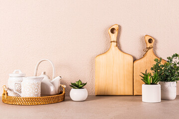 White ceramic tea set on round wicker tray among indoor plants on kitchen countertop. Kitchen background in light colors. A copy space. Front view