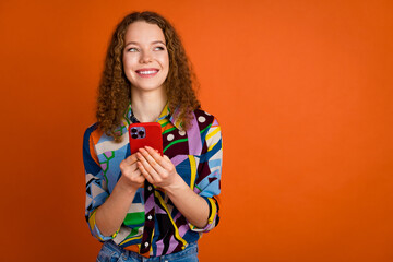Photo of cheerful pretty cute girl blogger wear trendy print clothes look empty space isolated on vibrant orange color background