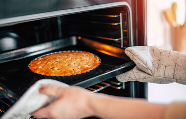 Close up image of woman hands using kitchen glove for taking sweet homemade dessert apple vegan pie out of oven in kitchen.