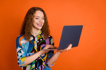Photo of adorable cheerful girl wear stylish print clothes use modern laptop isolated on vivid orange color background