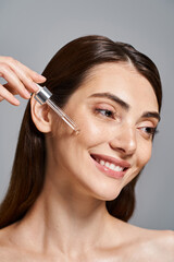 happy young woman with brunette hair smiles as she applying serum with cosmetic pipette in a studio setting.