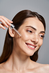 Fototapeta premium happy young woman with brunette hair smiles as she applying serum with cosmetic pipette in a studio setting.
