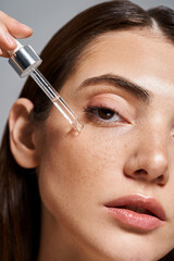 close up of young Caucasian woman with brunette hair and clean skin applying serum with cosmetic...