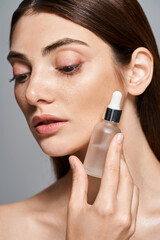 A young Caucasian woman with brunette hair and clean skin delicately holds a serum bottle of liquid in her hand.