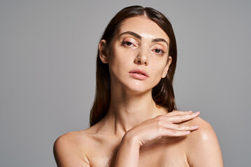 A young Caucasian woman with brunette hair confidently poses shirtless in a studio setting.