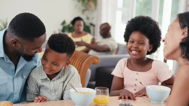 Family indoors at home at kitchen counter eating breakfast with grandparents in background - shot in slow motion