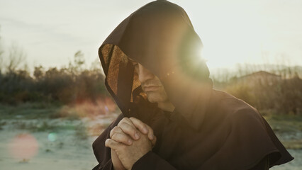 Religious Monk Wears His Hood And Prays In Nature At Sunset - obrazy, fototapety, plakaty
