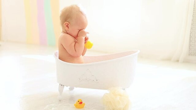 a little baby girl of six months is bathing in a bath with foam, soap is pinching the baby's eyes, bath foam got into the eyes of a child who is splashing in the water, the baby is washing