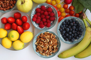 Apples, lemons, bananas, berries, carrots, leek, tomatoes, radishes, spinach and various nuts on white background. Healthy seasonal fruit and vegetable. Top view.