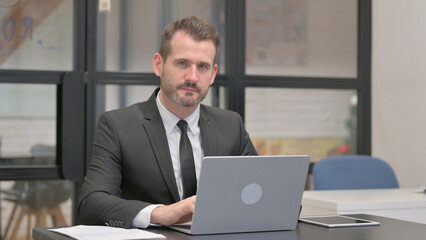 Businessman Looking at Camera while Working on Laptop