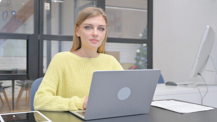 Young Blonde Woman Looking at Camera while Working on Laptop