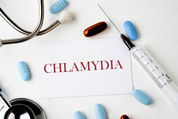 Medical concept. Word Chlamydia. on the card near the stethoscope, pills, syringe on a white...
